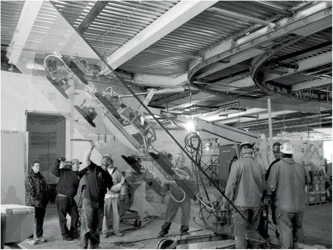 Glass panel being tilted in place on site. Curved steel tracks for glass are exposed below the roof until the ceiling conceals them